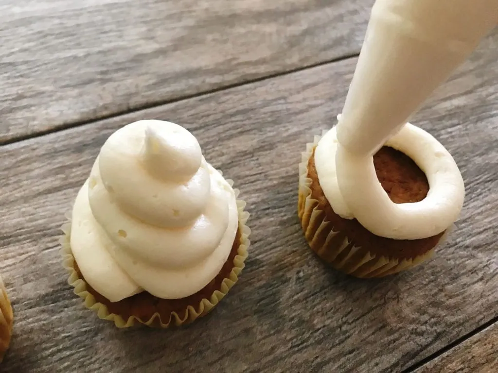 White frosting being swirled on cupcakes to make Halloween Cupcakes.