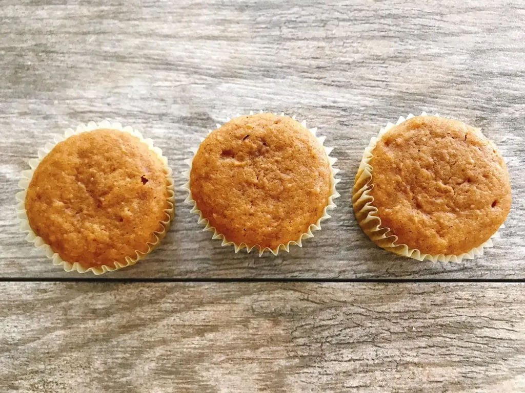 Three pumpkin spice cupcakes on a wood background to make Halloween Cupcakes.