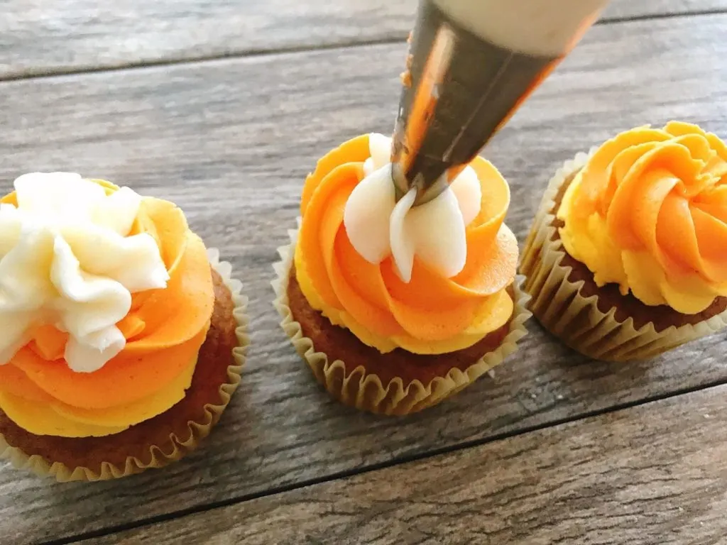 A piping bag piping a star on top of a candy corn cupcake to make Halloween Cupcakes.