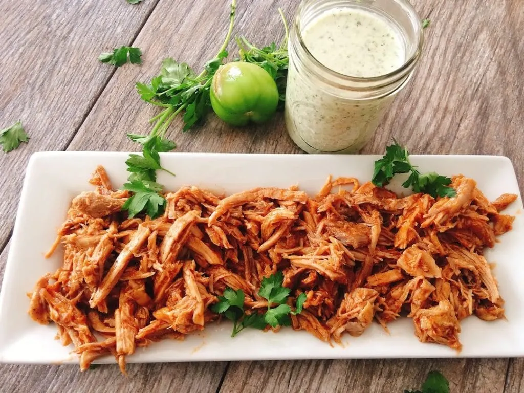A plate of pulled Sweet Pork Barbacoa sprinkled with cilantro with a jar of creamy cilantro lime ranch.