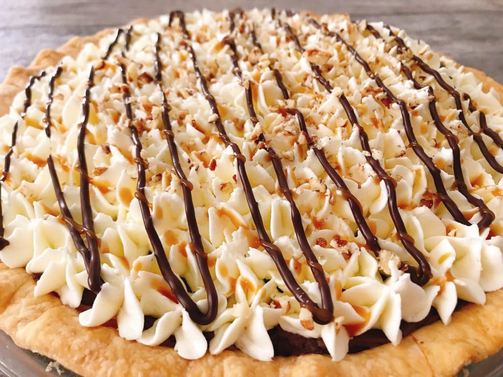 A close up of a Caramel Pecan Silk Pie drizzled with chocolate, caramel, and sprinkled with pecans.