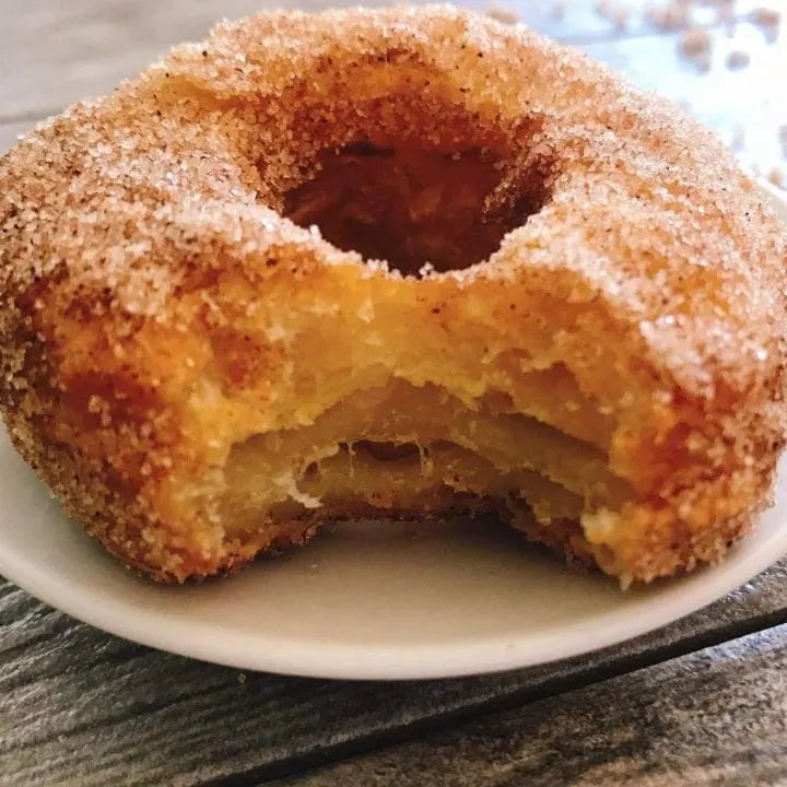 A freshly fried Disney World cronut on a white plate covered in cinnamon and sugar.