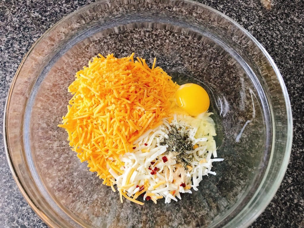 Shredded cheese, spices and an egg in a bowl to make Keto Pizza.