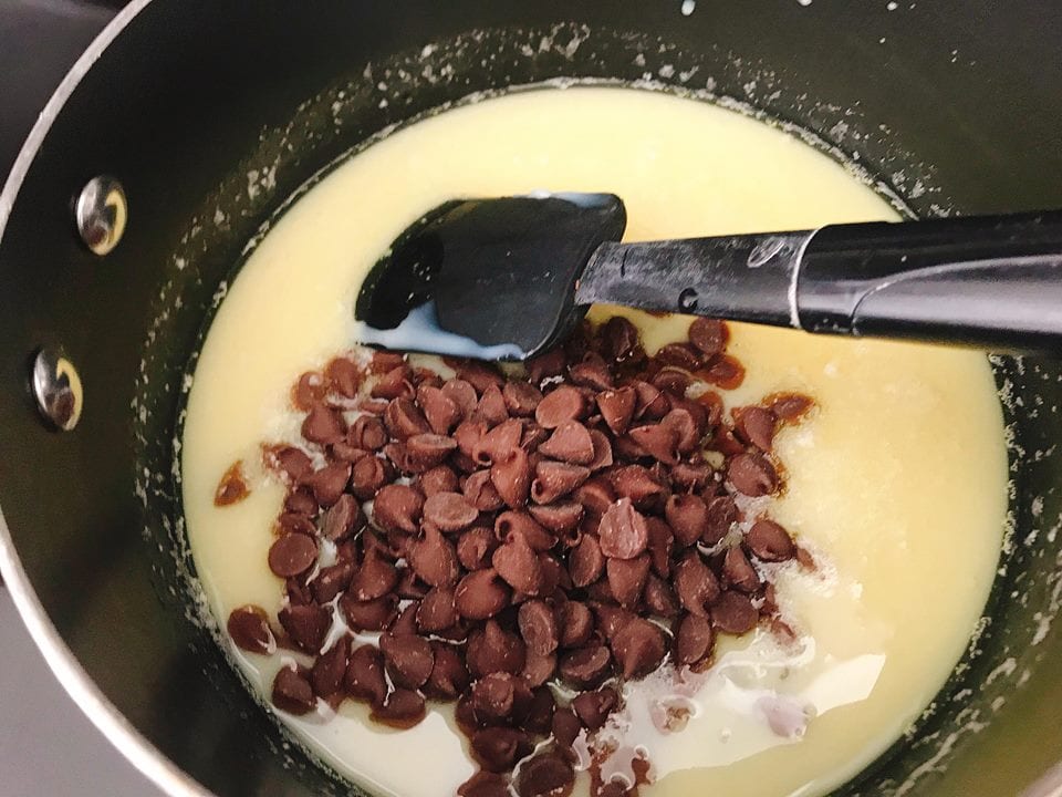 Chocolate chips, melted butter, and sweetened condensed milk in a saucepan with a spatula.