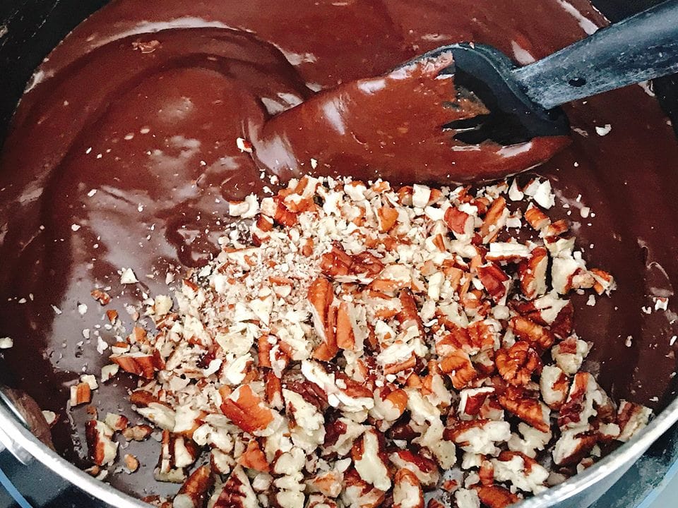 Chopped pecans being stirred into melted chocolate to make easy homemade fudge recipe.