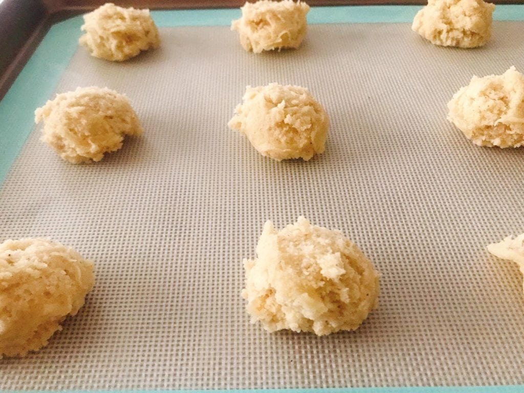 Balls of unbaked Frosted Eggnog Cookie Dough lined up on a baking sheet.