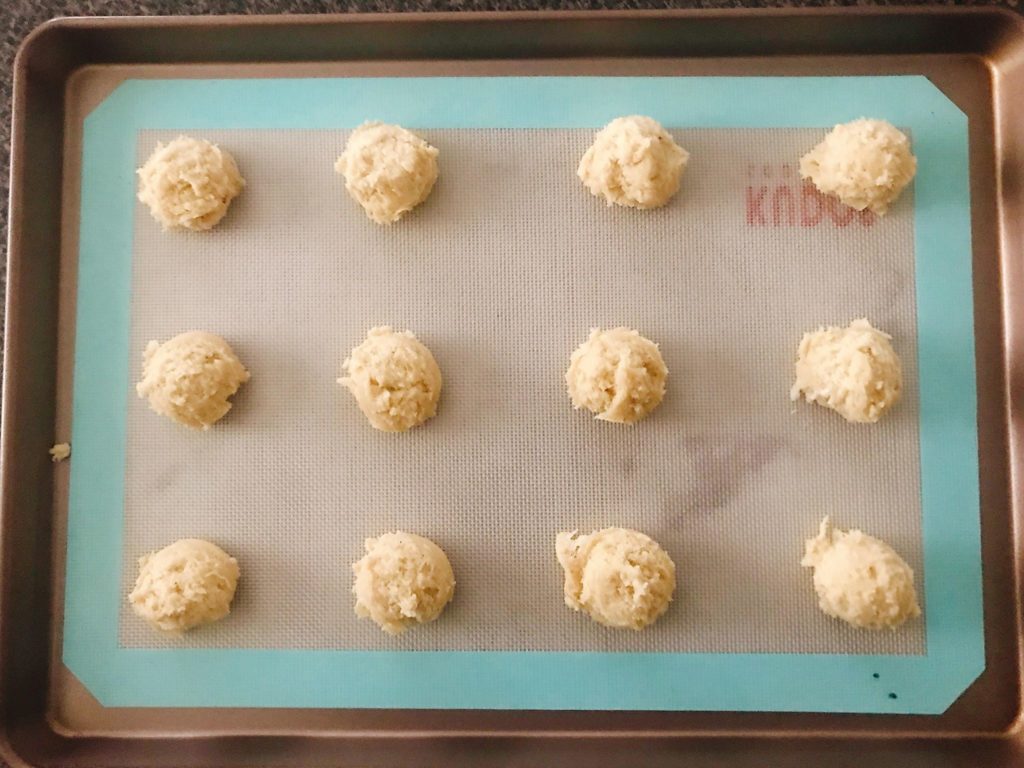 A top view of balls of unbaked Frosted Eggnog Cookie Dough lined up on a baking sheet.