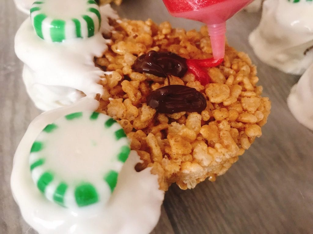 A Mickey Mouse Gingerbread Rice Krispie Treat being decorated with red decorating gel.