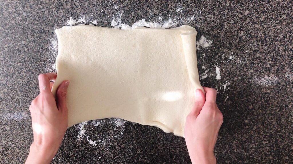 Pizza dough being spread out on a counter top