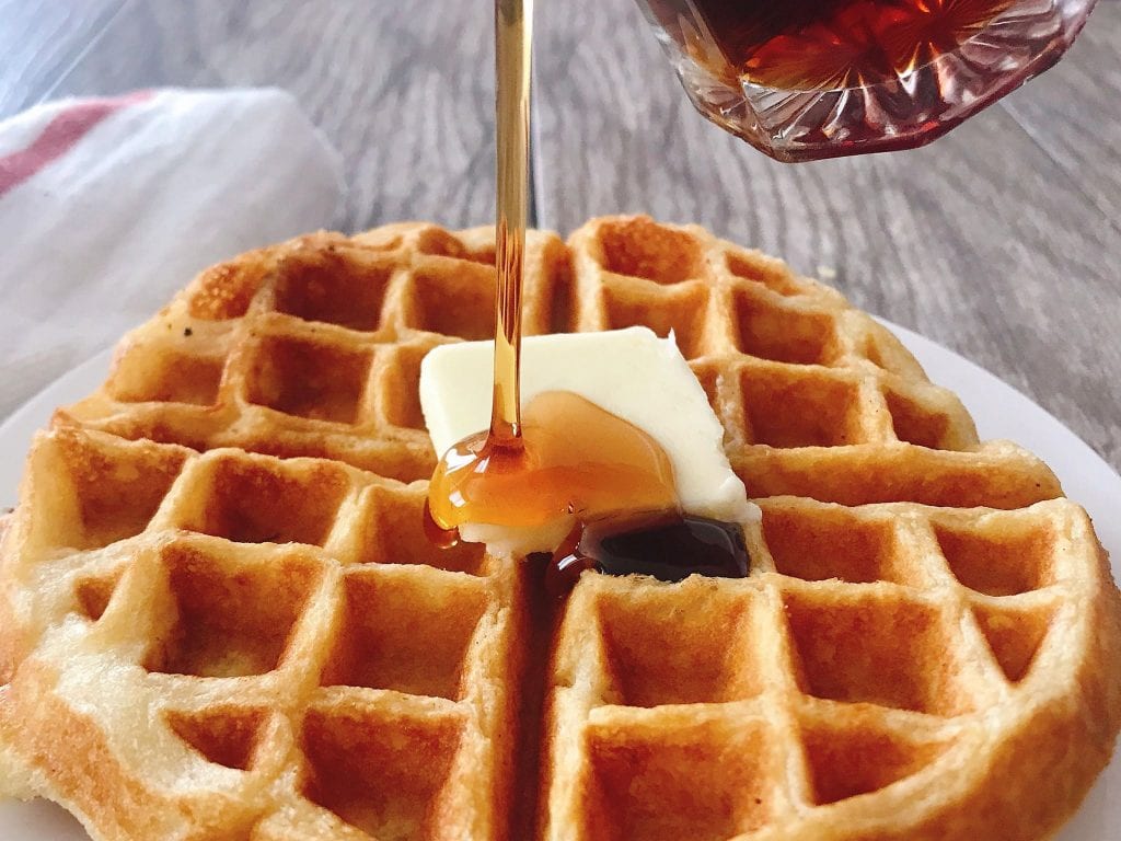 Syrup being poured on Sweet Cream Waffles with butter.
