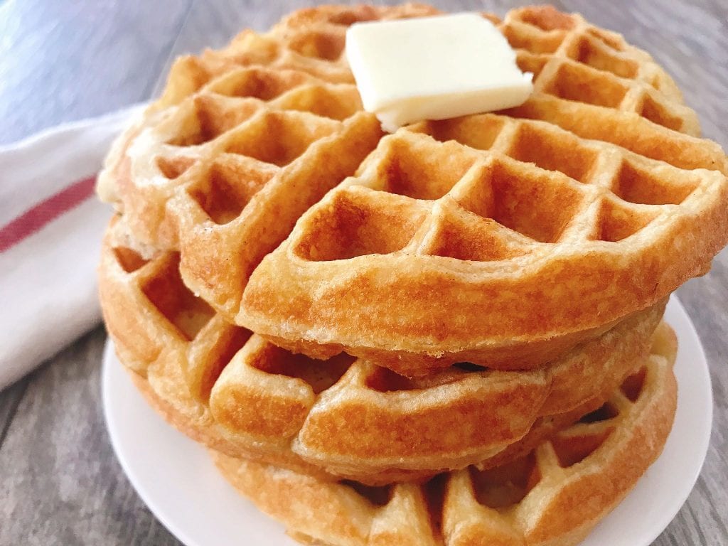 A stack of sweet cream waffles on a plate with a pat of butter.