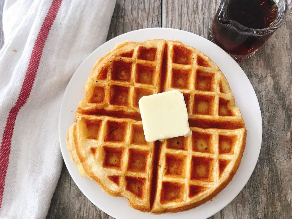 A waffle on a plate with a pat of butter.