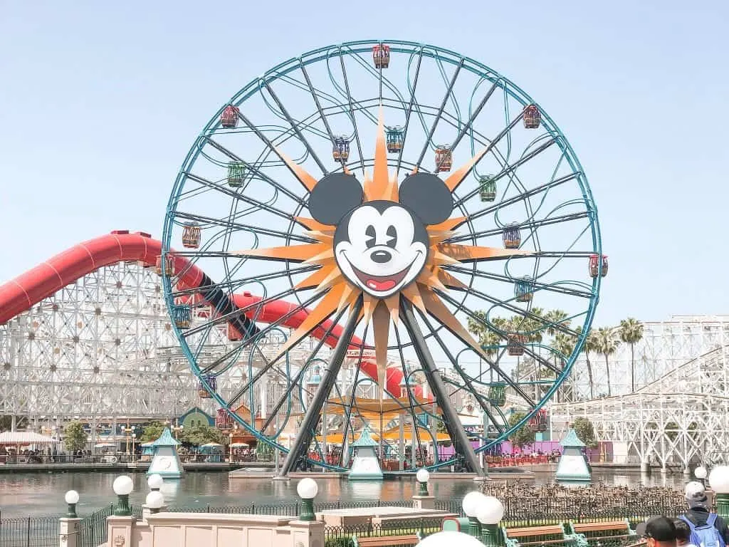 Mickey Mouse face on a Ferris wheel in front of a white roller coaster at Disneyland.