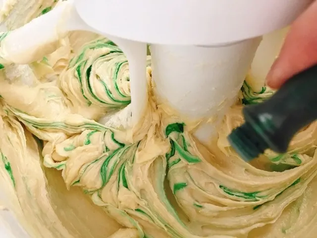 Green food coloring being poured into cookie dough.