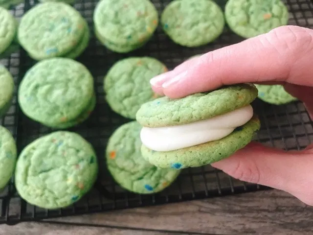 A hand holding a Shamrock Shake Whoopie Pie with white cream filling.