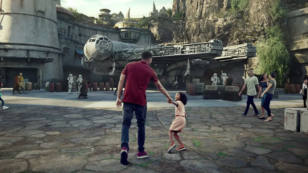 A dad and his daughter holding hands in front of Star Wars: Galaxy's Edge the new Star Wars Land in Disneyland and Walt Disney World.