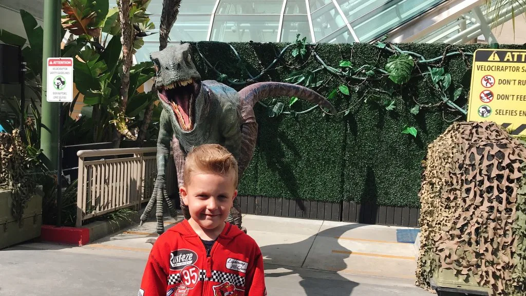 A boy standing in front of a robotic velociraptor at Universal Studios Hollywood.