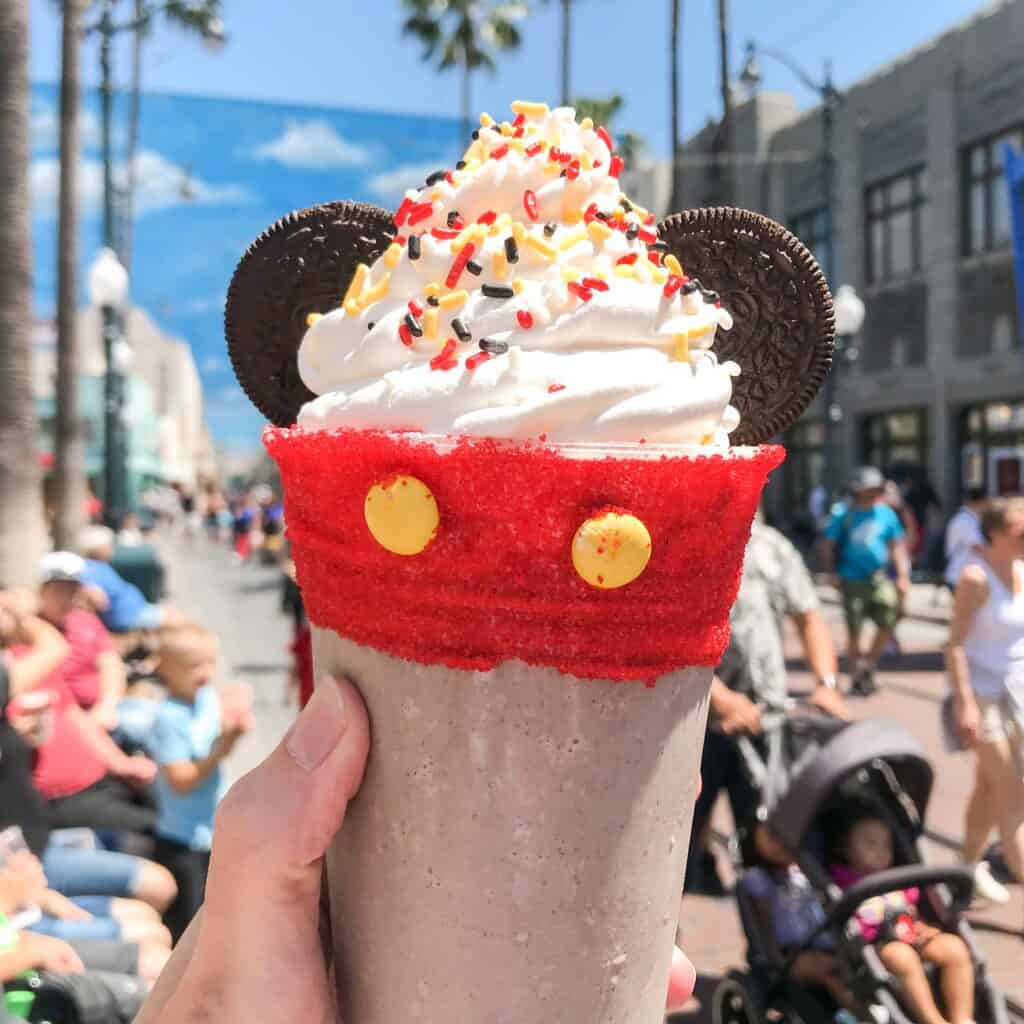 A milkshake in a cup decorated to look like Mickey Mouse pants with cookie Ears.