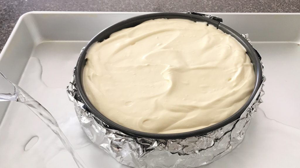 Cheesecake batter in a springform pan, placed in a roasting pan being filled with water.