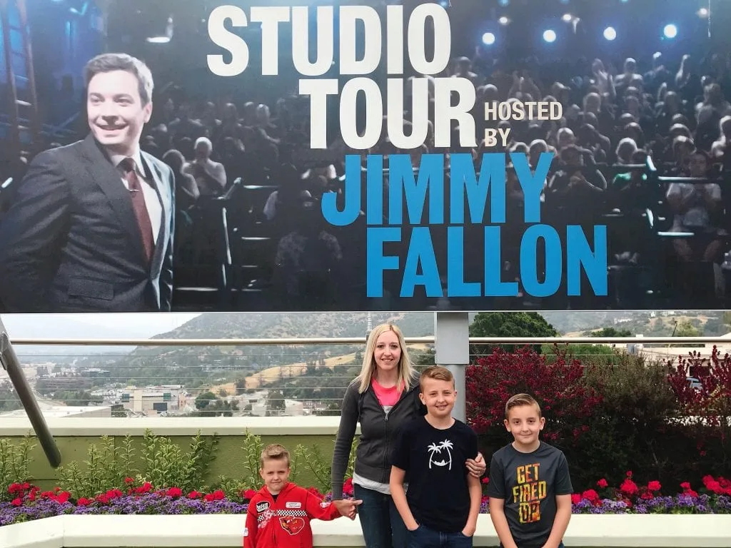 A family with a sign of Jimmy Fallon that says “Studio Tour Hosted By Jimmy Fallon”