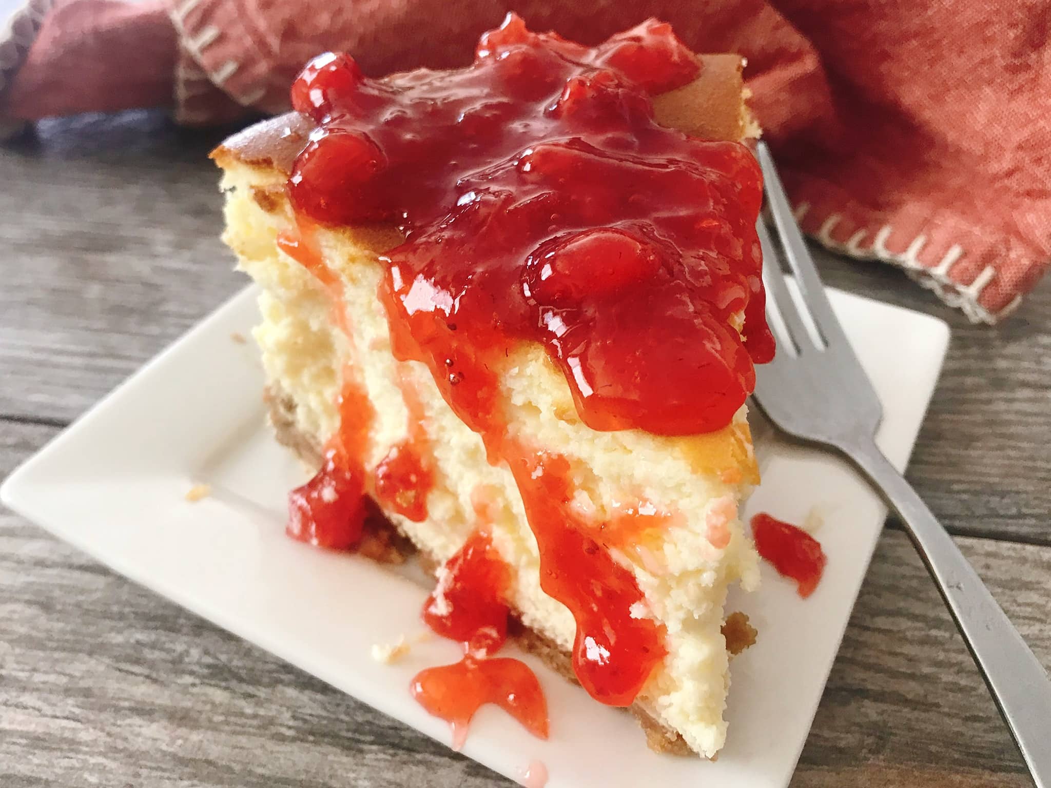 A slice of classic New York cheesecake topped with strawberry sauce.