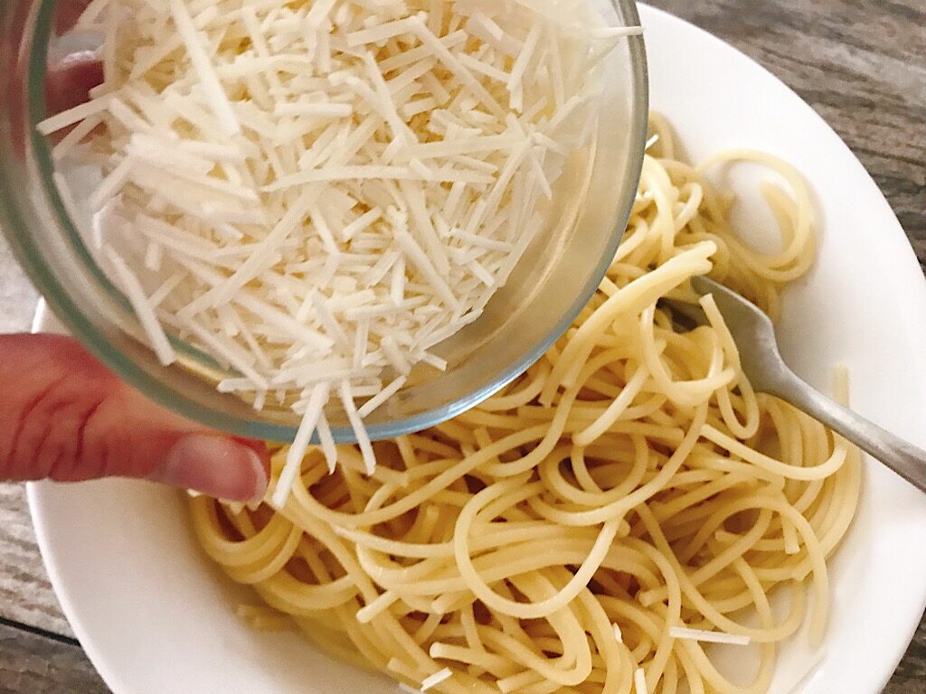 A bowl of Mizithra cheese being poured over a bowl of spaghetti