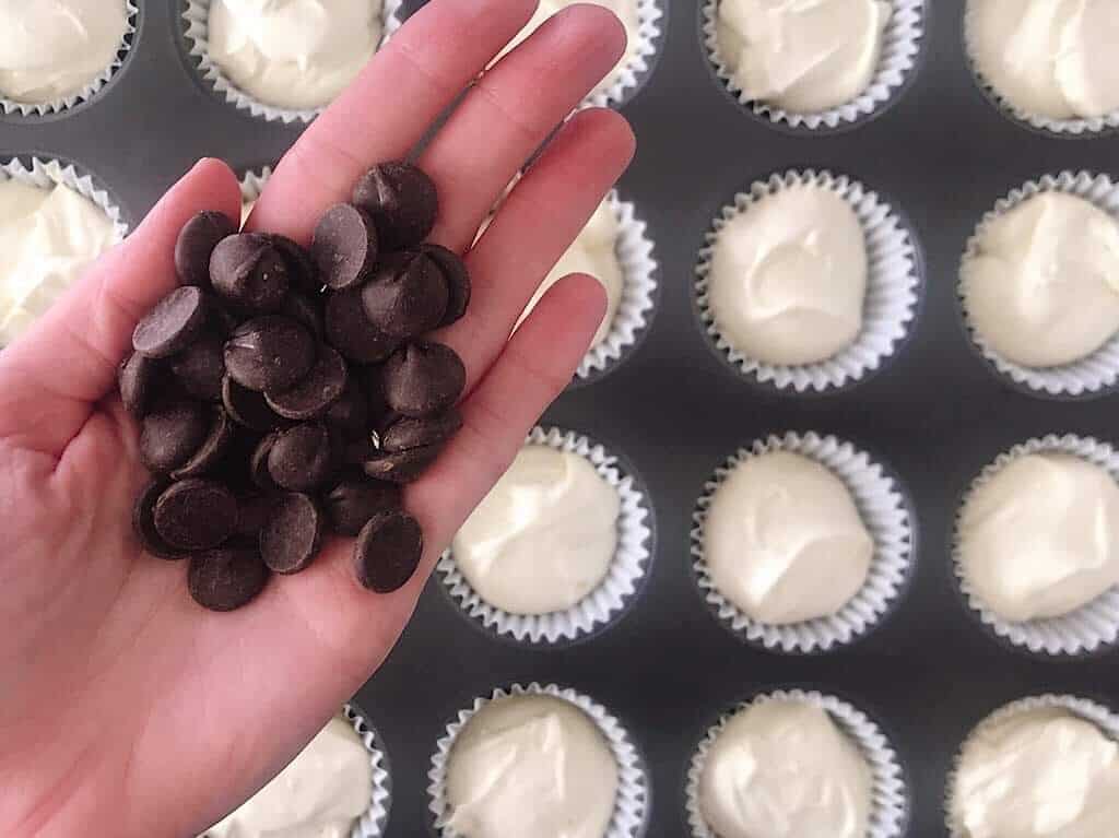 A hand holding chocolate chips over cheesecake bites batter.