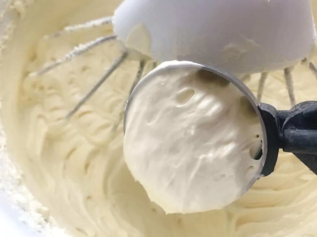 A scoop of cheesecake batter over a mixing bowl of batter.