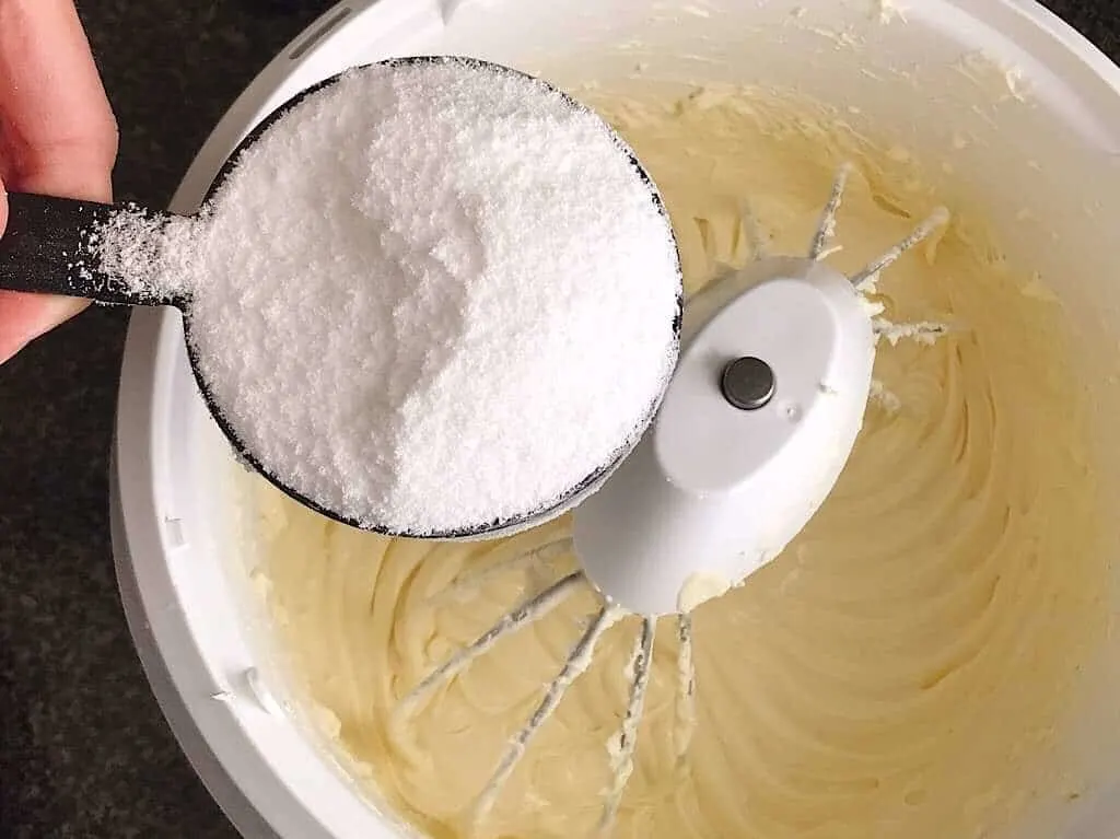 A cup of stevia over a mixing bowl of cheesecake batter.