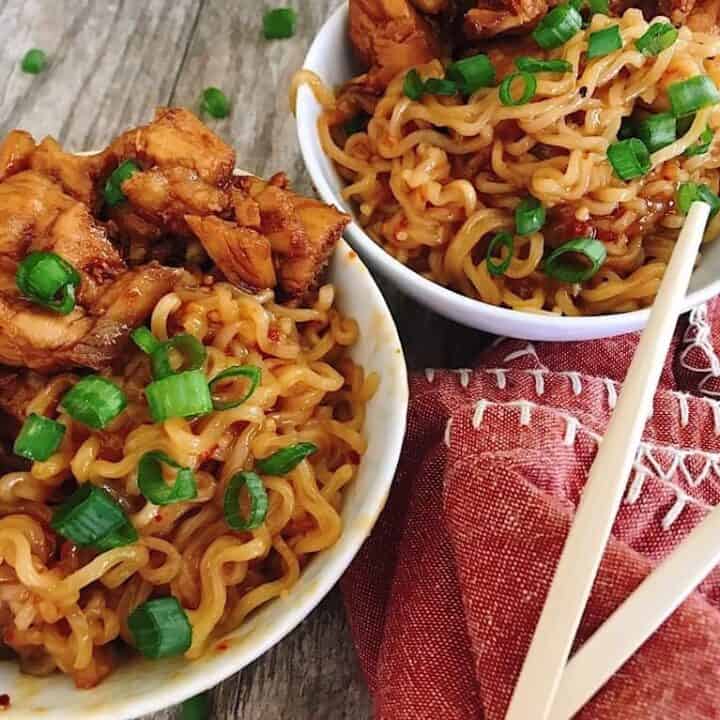 Two bowls of noodles with chicken and chopsticks.