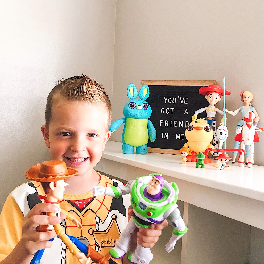 A boy in a Woody shirt playing with Woody and Buzz Lightyear in front of more toys and a sign that says, “You’ve got a Friend in Me.”