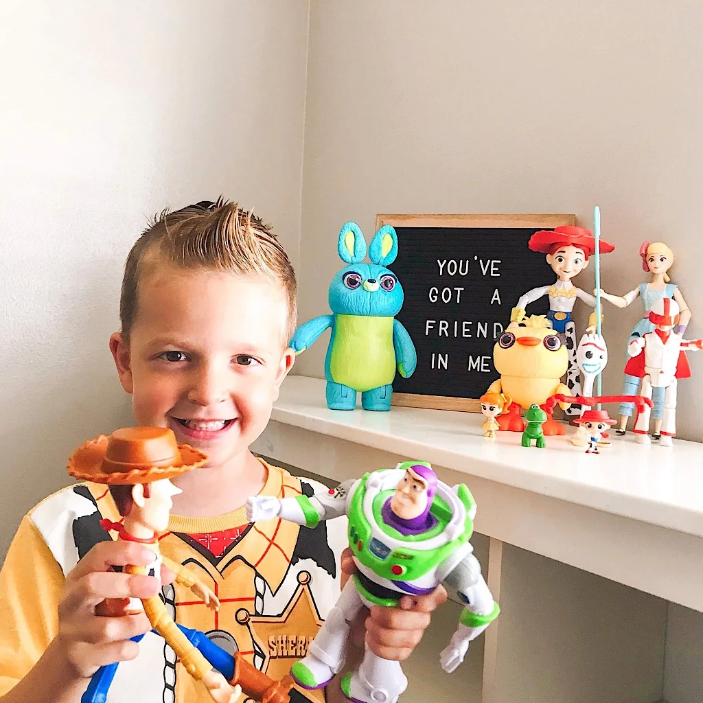 A boy in a Woody shirt playing with Woody and Buzz Lightyear in front of more toys and a sign that says, “You’ve got a Friend in Me.”