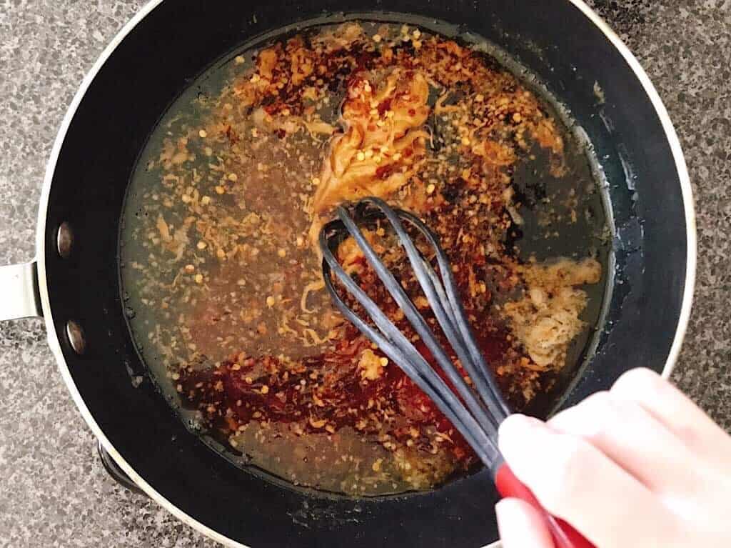 A whisk stirring sauce in a pan.