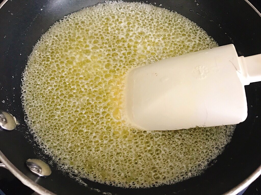 A spoon stirring a pan of boiling butter.
