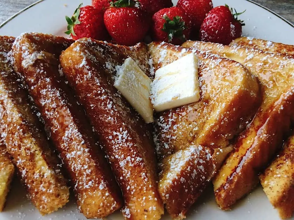 Slices of Perfect French Toast lined up with butter and strawberries.