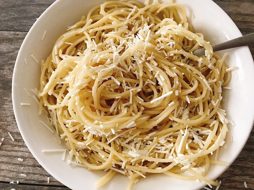 A bowl of browned butter spaghetti with Mizithra cheese and a fork.