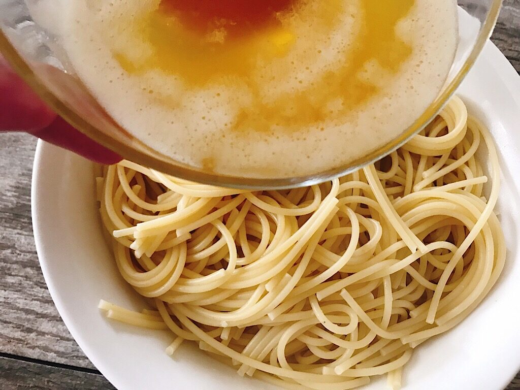 A bowl of browned butter being poured over a bowl of spaghetti.