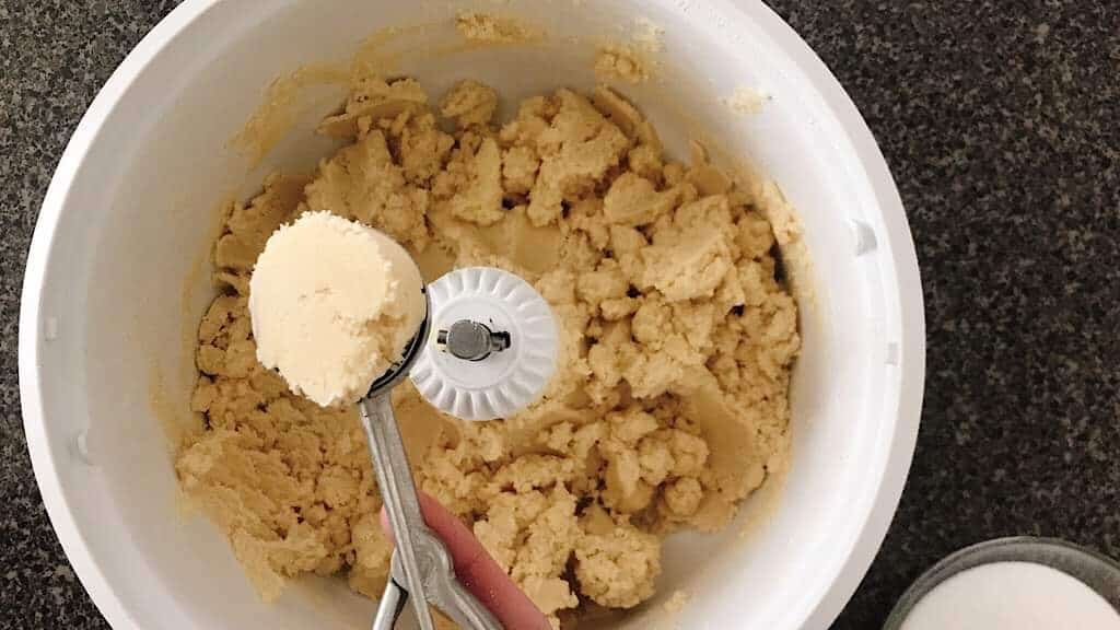 A cookie scoop with a ball of sugar cookie dough over a mixing bowl.