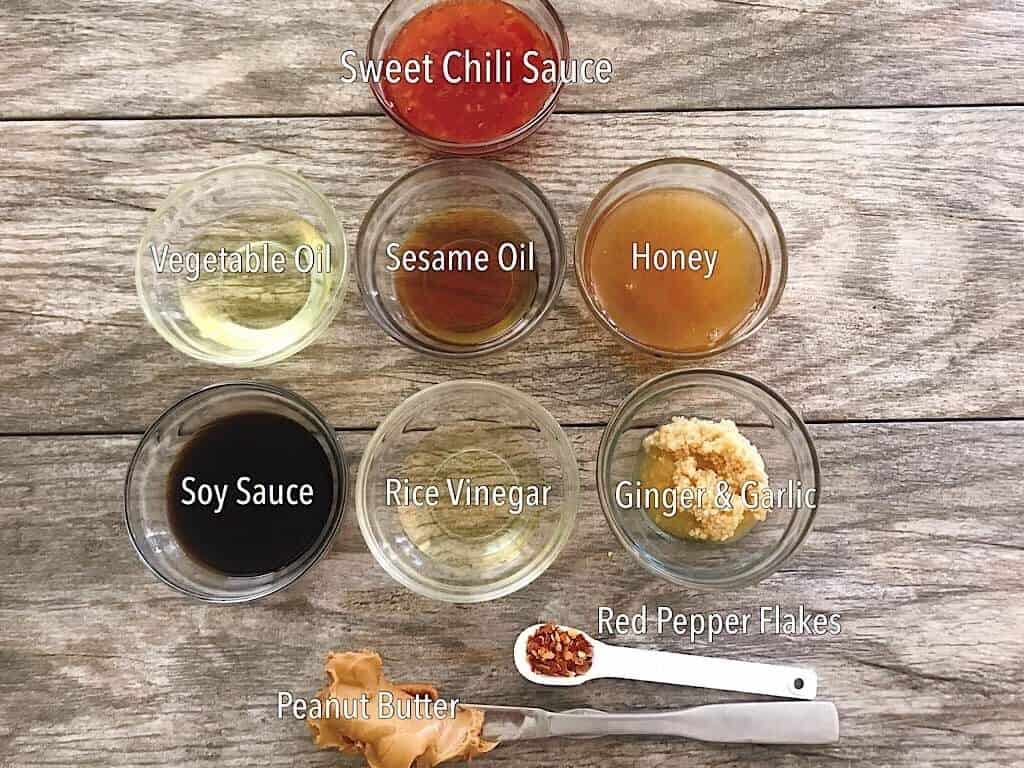 Small bowls filled with sweet chili sauce, vegetable oil, sesame oil, honey, soy sauce, rice vinegar, ginger, garlic, red pepper flakes, and peanut butter.