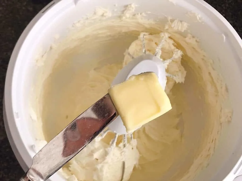 A pat of butter on a knife over a bowl of cheesecake batter.