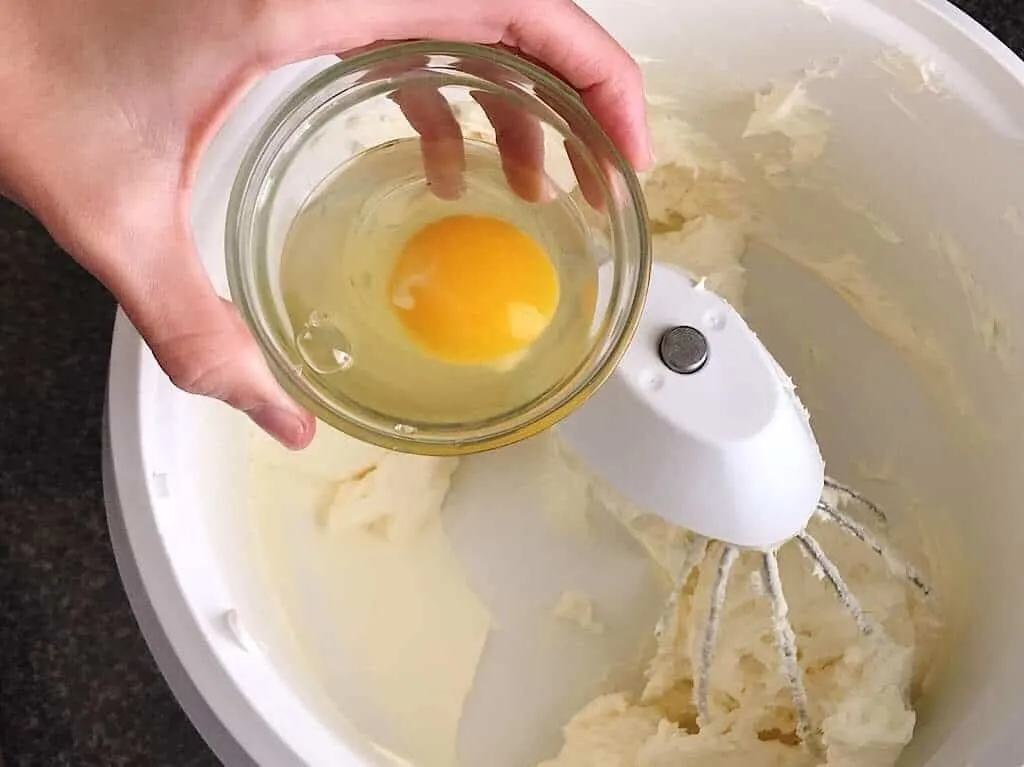 An egg in a bowl over a mixing bowl of low carb cheesecake batter.