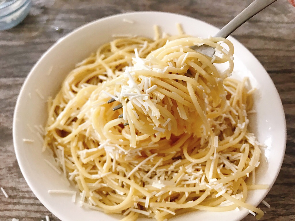 A fork full of pasta over a bowl of spaghetti topped with browned butter sauce and Mizithra cheese.