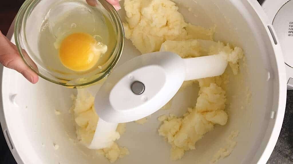 An egg being added to a mixing bowl.