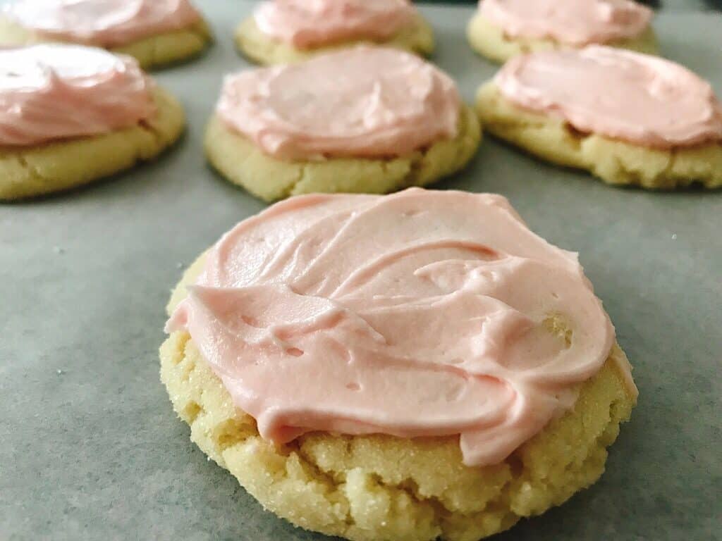 A close up photo of soft and chewy sugar cookies with pink frosting.