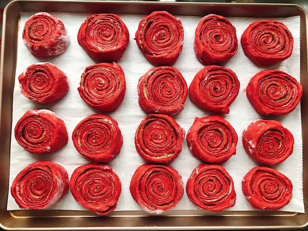 Unbaked red velvet cinnamon rolls on a baking sheet.