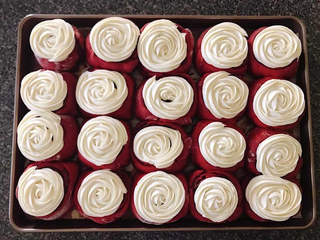 A pan of red velvet cinnamon rolls with cream cheese frosting.