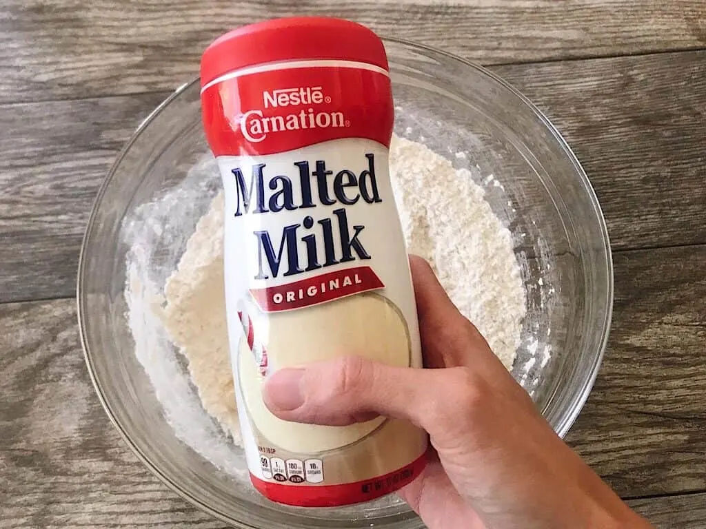 A container of Malted Milk over a bowl of flour.