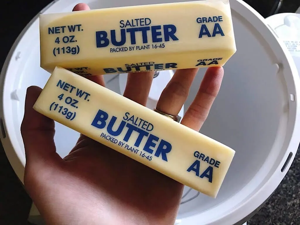 Two sticks of butter being held over a stand mixer to make cream cheese frosting