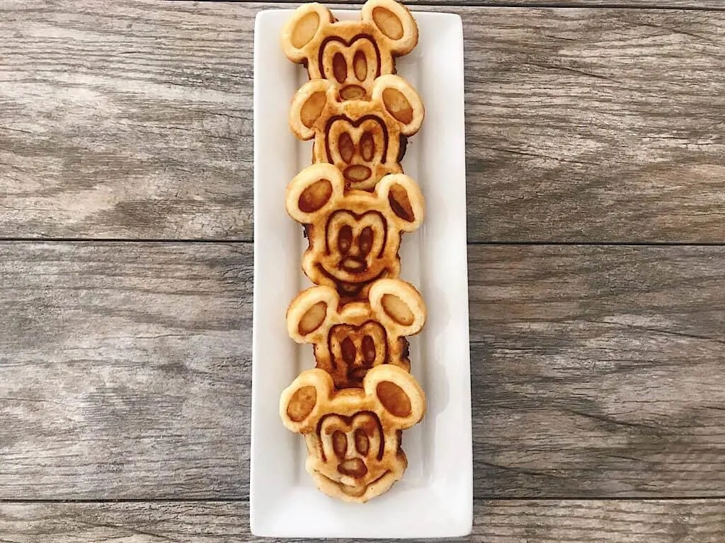 Mickey Mouse shaped waffles lined up on a white plate.