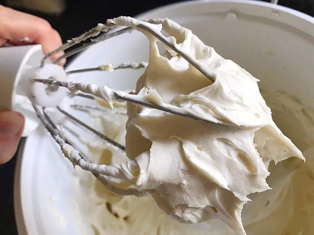 Cream cheese buttercream frosting on the whisk attachment of a stand mixer.